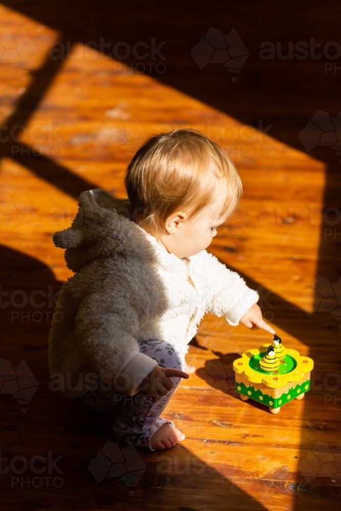 Bright sunlight falling on child playing on wooden floorboard floor in home - Australian Stock Image