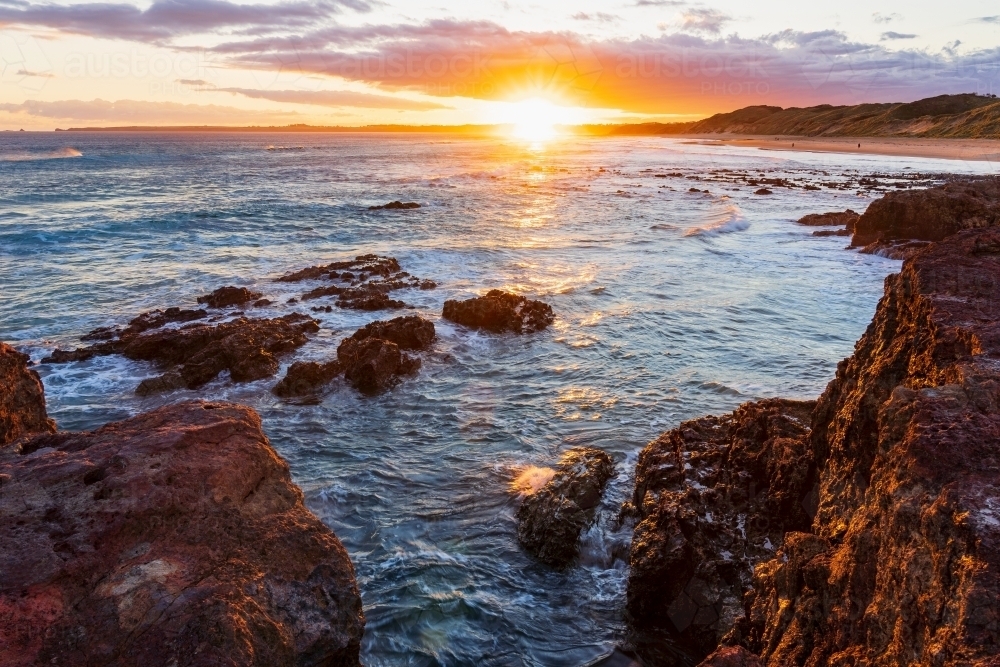 Bright sunset over a rocky coastline with gentle waves - Australian Stock Image