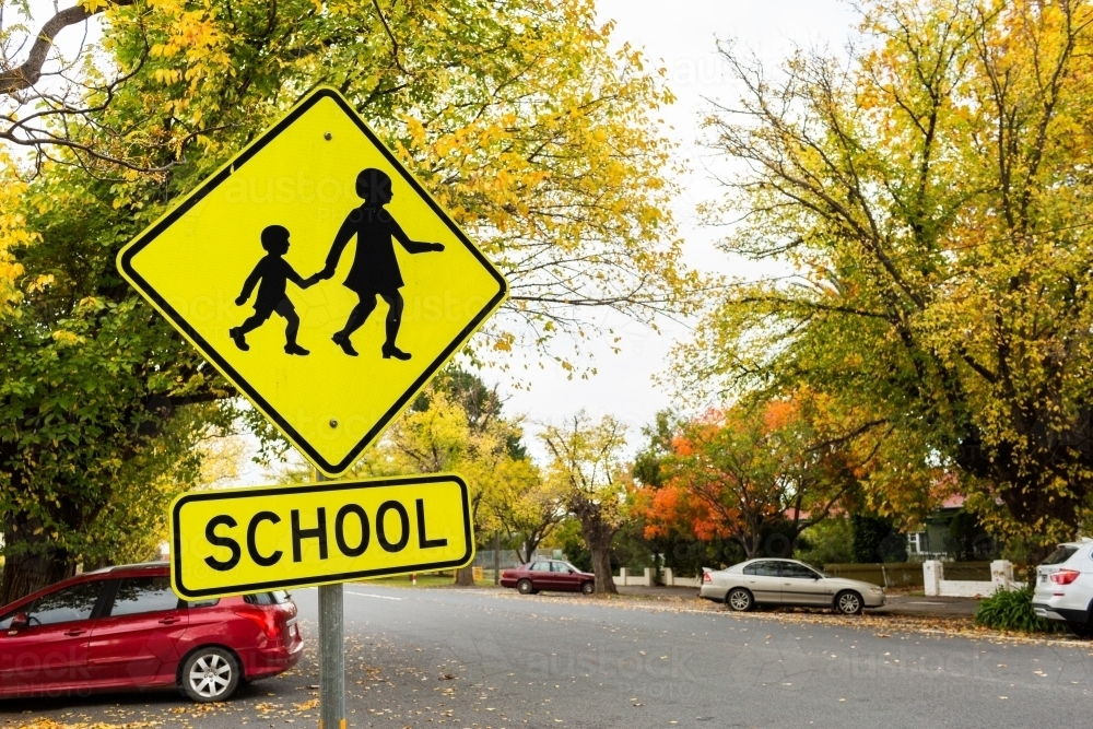 Bright yellow school sign in Autumn street with parked cars - Australian Stock Image