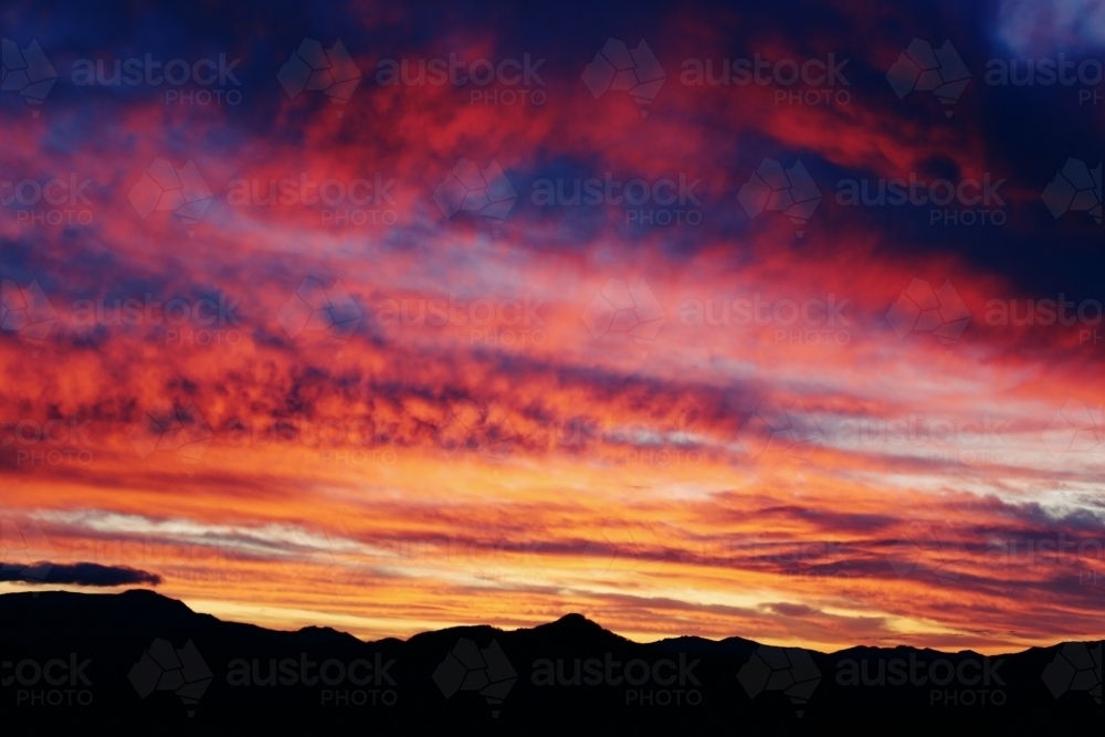 Brightly coloured sunset above mountains - Australian Stock Image