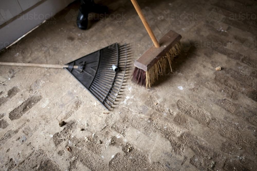 Broom and rake lying on old brick floor - Australian Stock Image