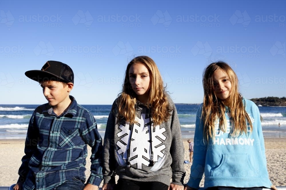 Brother and his sisters sitting on a railing at the beach - Australian Stock Image
