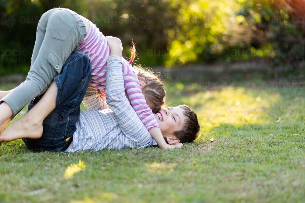 Brother and sister play fighting together on lawn in garden - Australian Stock Image