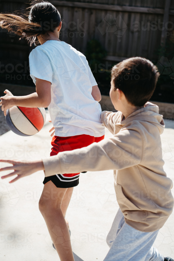 Brother and sister playing basketball in their yard together - Australian Stock Image