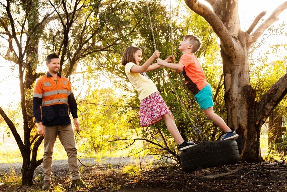 Brother and sister playing on tyre swing in front yard - Australian Stock Image