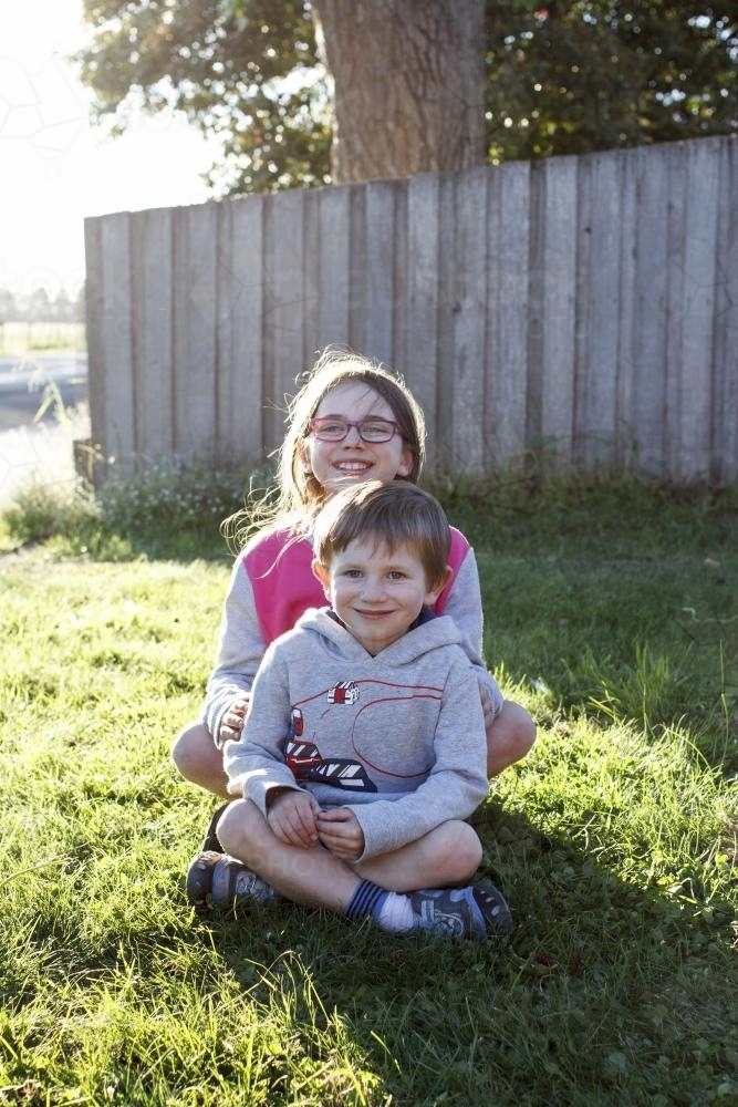 Brother and Sister sitting on green grass in afternoon sun - Australian Stock Image