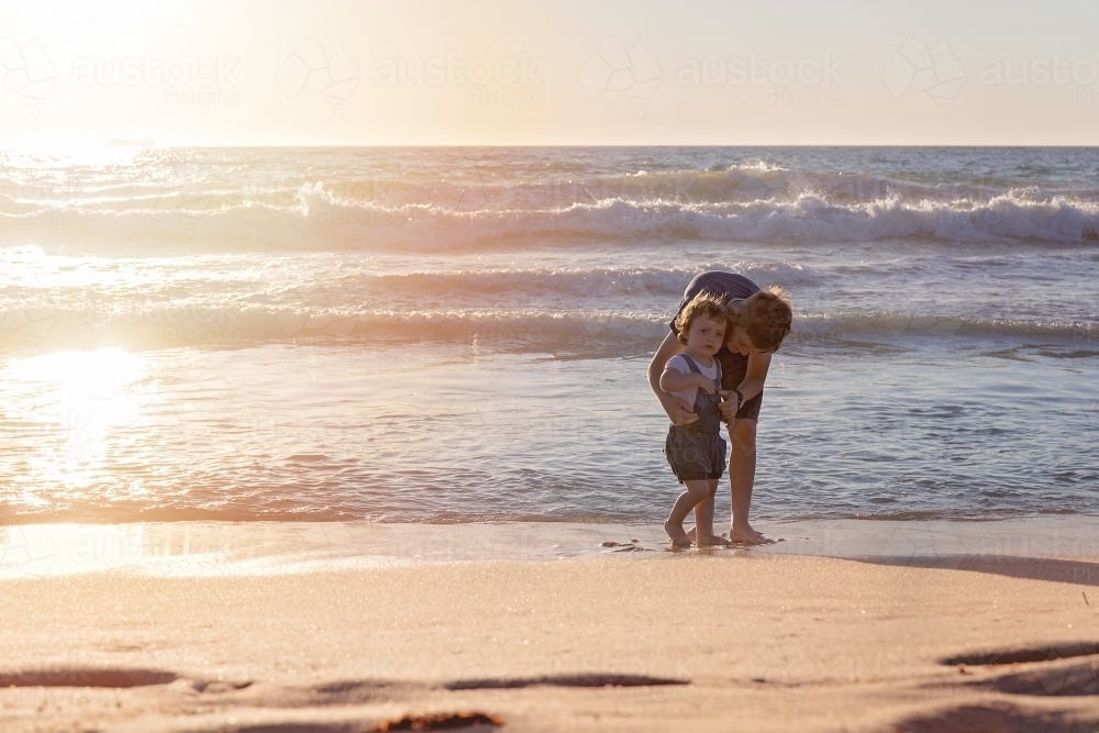 Brother Caring for His Sister On The Beach At Sunset - Australian Stock Image