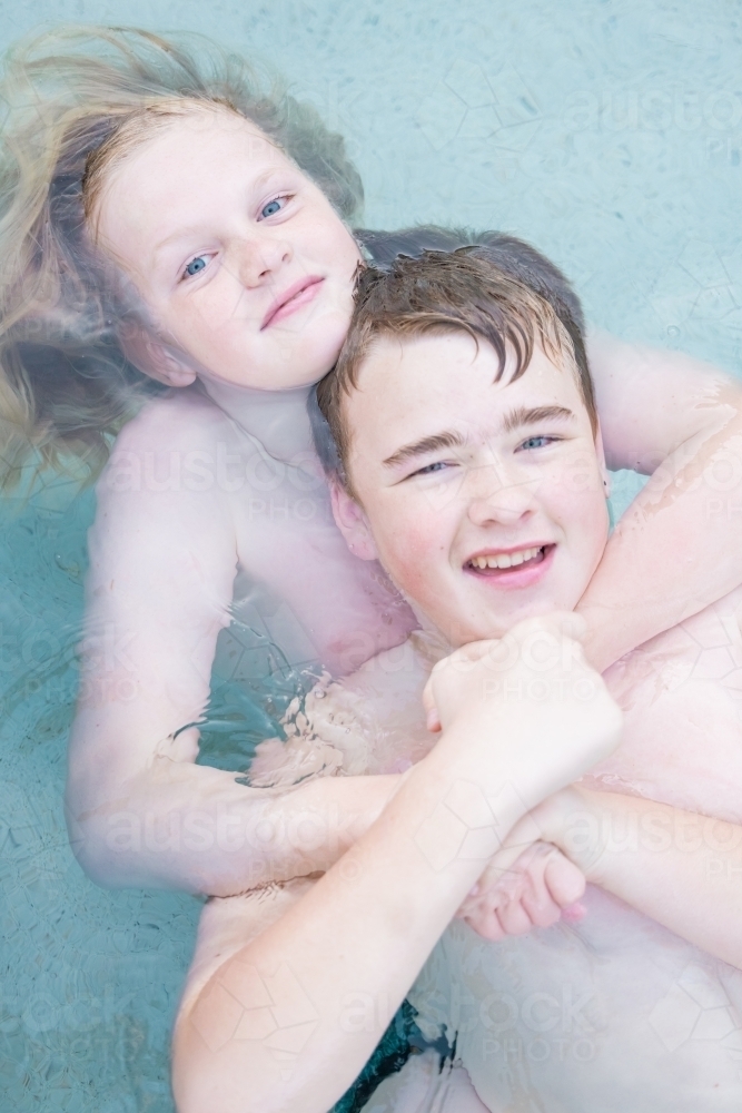 Brothers floating together in swimming pool - Australian Stock Image