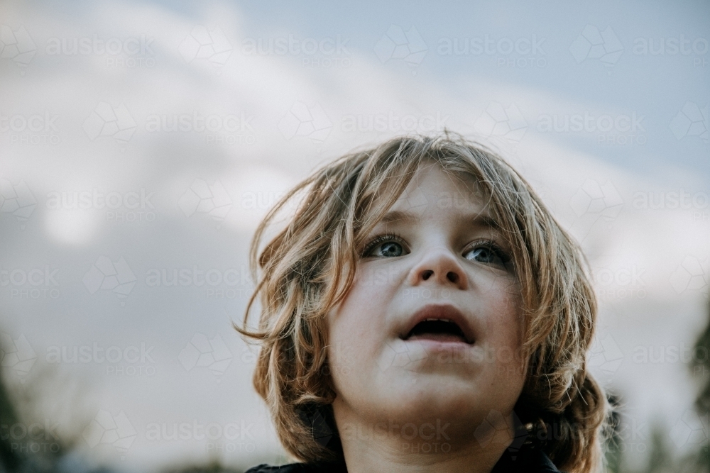 Close up of young boy outside looking off into the distance - Australian Stock Image