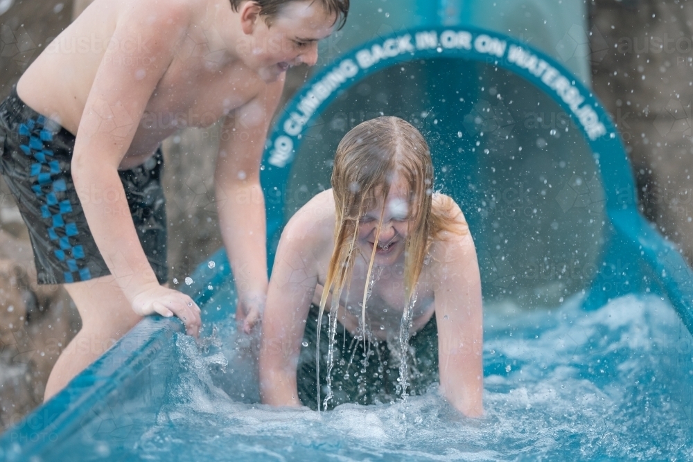 Brothers playing at the bottom of a waterslide on holiday - Australian Stock Image