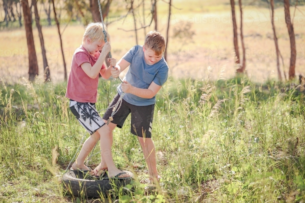 Brothers playing on broken rope swing in natural bush setting - Australian Stock Image