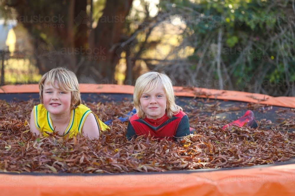 Brothers playing on trampoline covered in fallen leaves in Autumn - Australian Stock Image