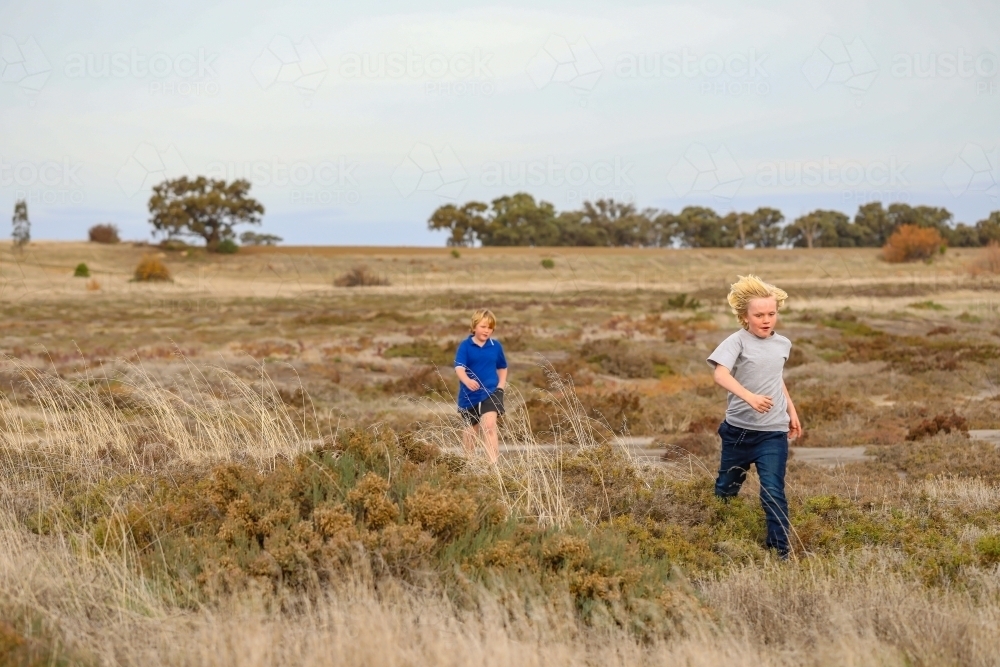 Brothers running while exploring desolate dry lake together. Family outing in the Australian bush. - Australian Stock Image