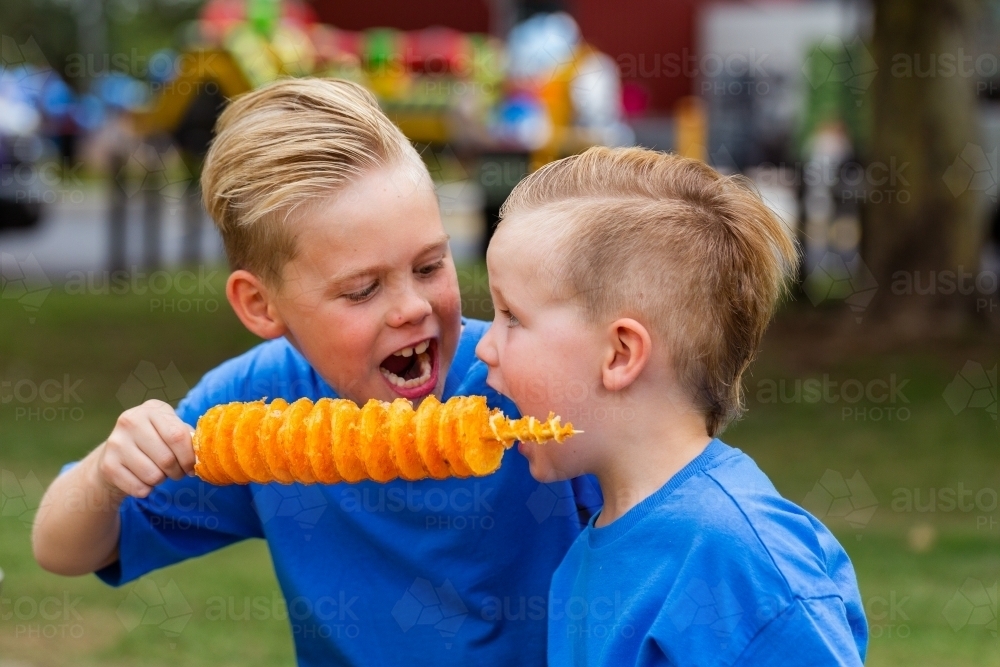 brothers sharing hot flavoured chips on a stick – Potato Spirals to eat - Australian Stock Image