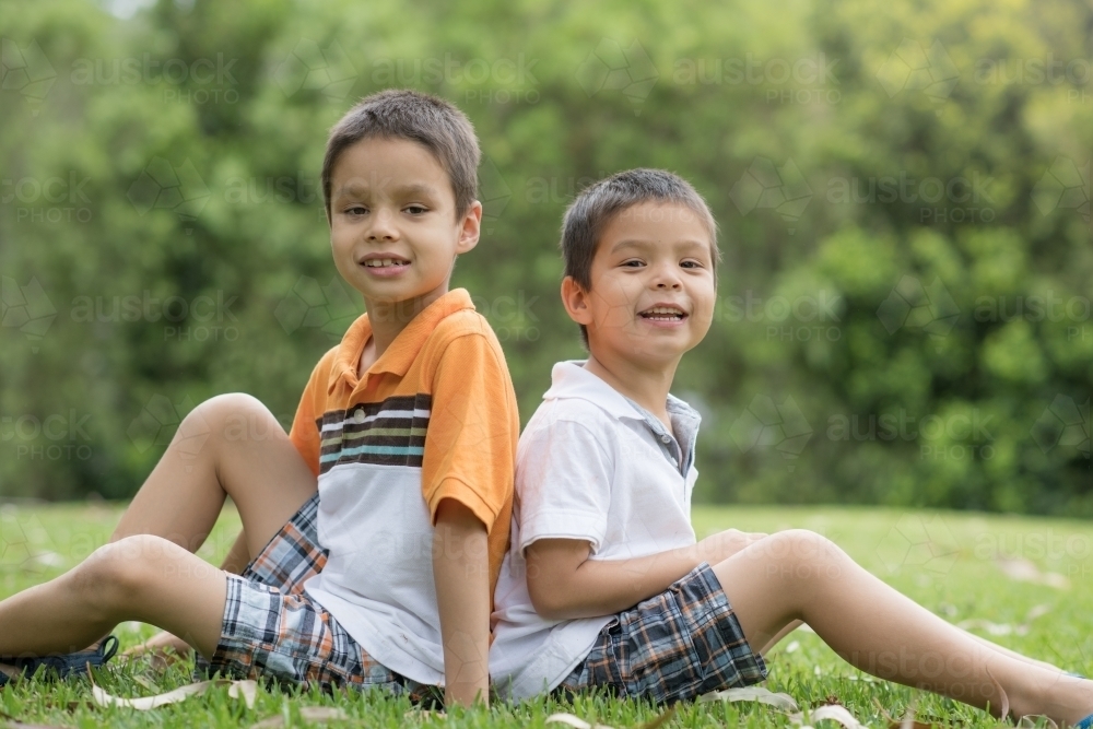 Brothers sit back to back outside - Australian Stock Image