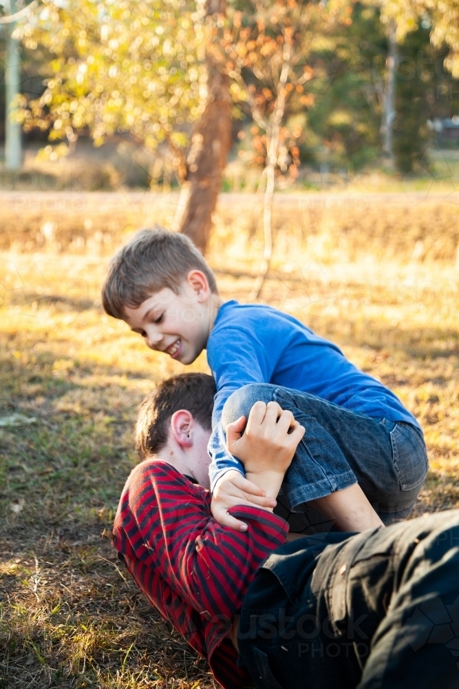 Brothers tackle wrestling each other outside - Australian Stock Image