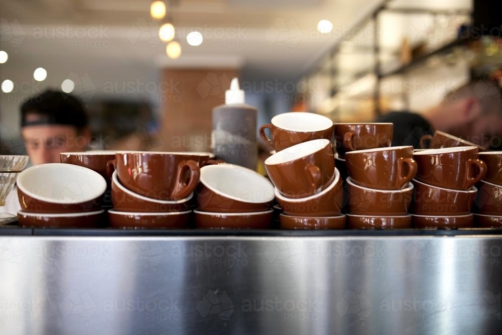 Brown coffee cups stacked on coffee machine at cafe - Australian Stock Image