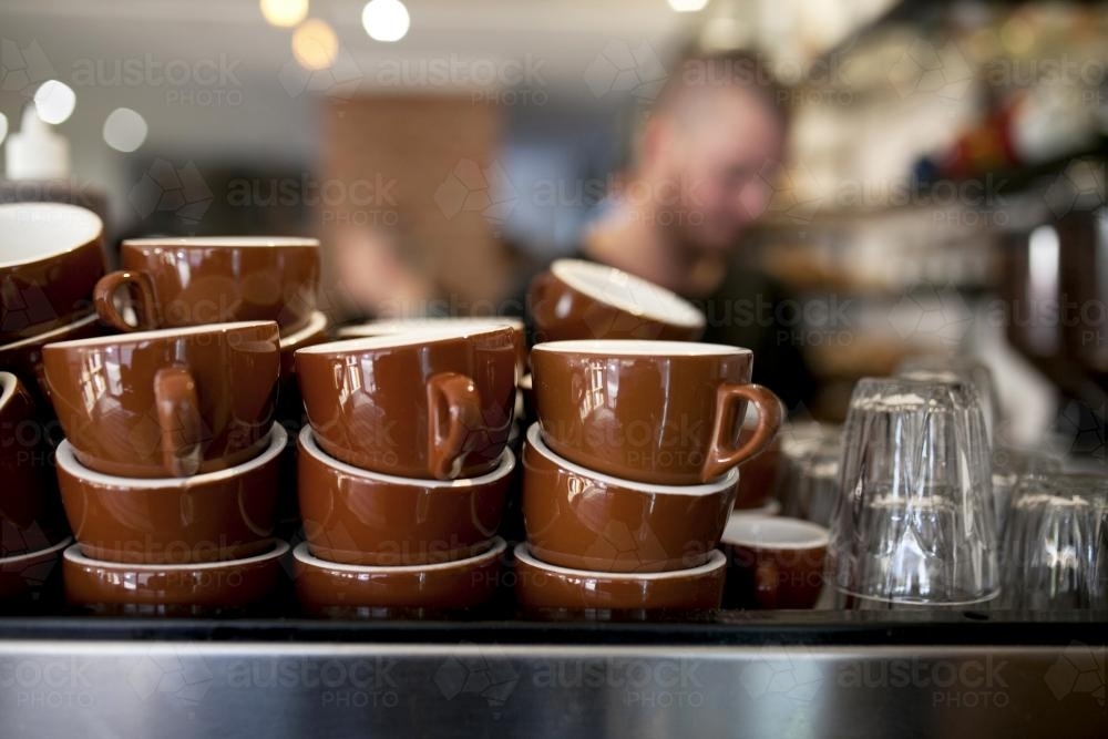 Brown coffee cups stacked on coffee machine at cafe - Australian Stock Image