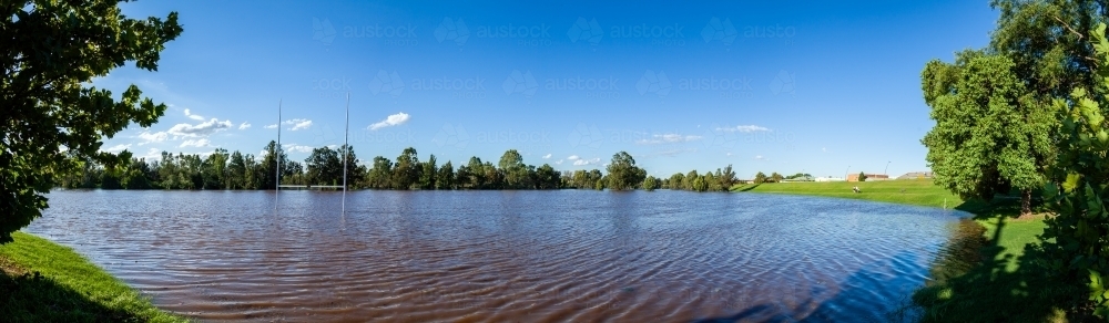Brown floodwaters covering park playing field after river broke banks - Australian Stock Image