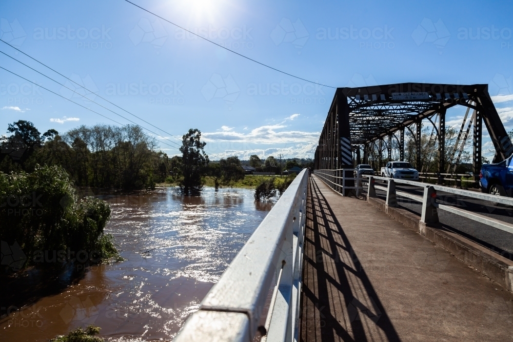 Brown floodwaters rising under bridge with pedestrian crossing footparh - Australian Stock Image