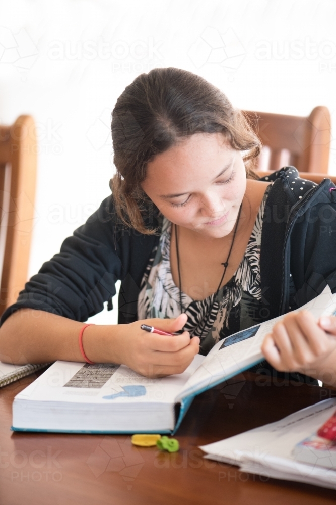 Brown haired teenager sitting at dining table studying intently. - Australian Stock Image