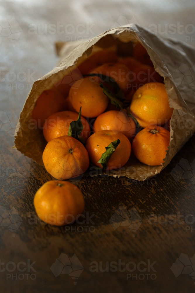 Brown paper bag overflowing with mandarins on wooden table - Australian Stock Image