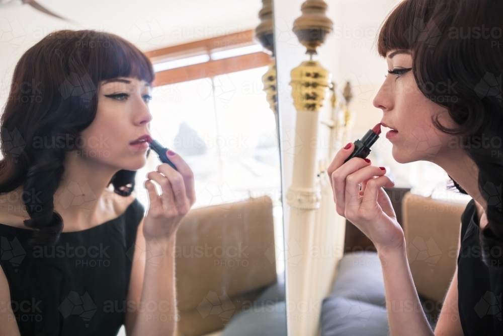 Brunette woman applying red lipstick in preparation for a formal event - Australian Stock Image