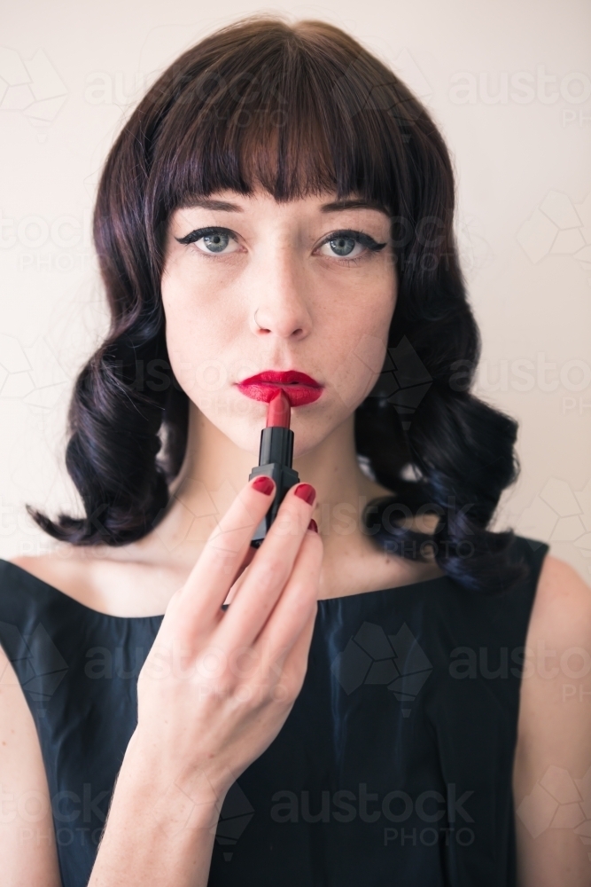 Brunette woman holding red lipstick to her lips staring into camera - Australian Stock Image