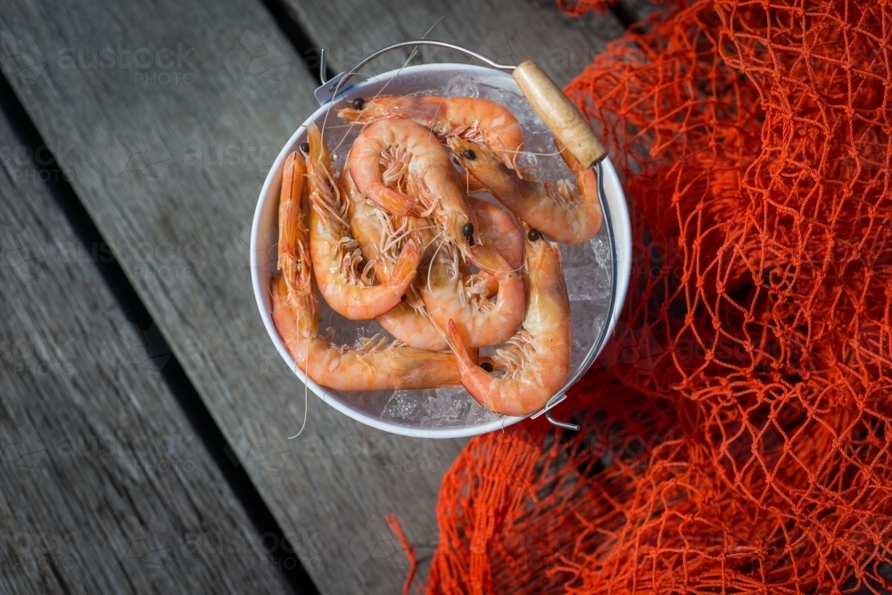 Bucket of prawns on ice, sitting next to red netting - Australian Stock Image