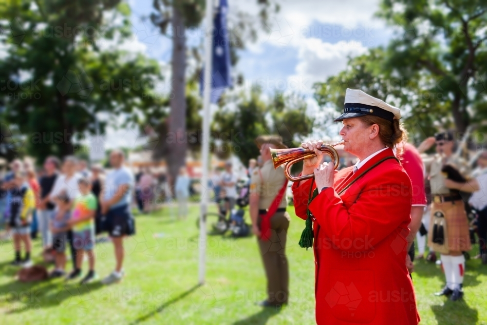 Bugle player playing at ANZAC day memorial service with blur of crowd in background - Australian Stock Image