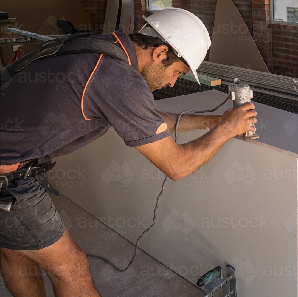Builder wearing hard hat & tool belt using router on door - Australian Stock Image