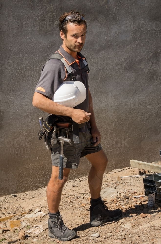 Builder with hard hat, tool belt & safety goggles standing outside - Australian Stock Image
