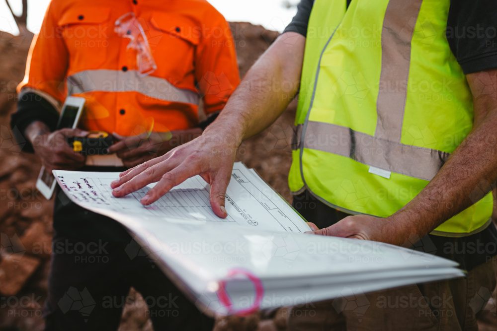 Builders holding a blueprint at the construction site. - Australian Stock Image
