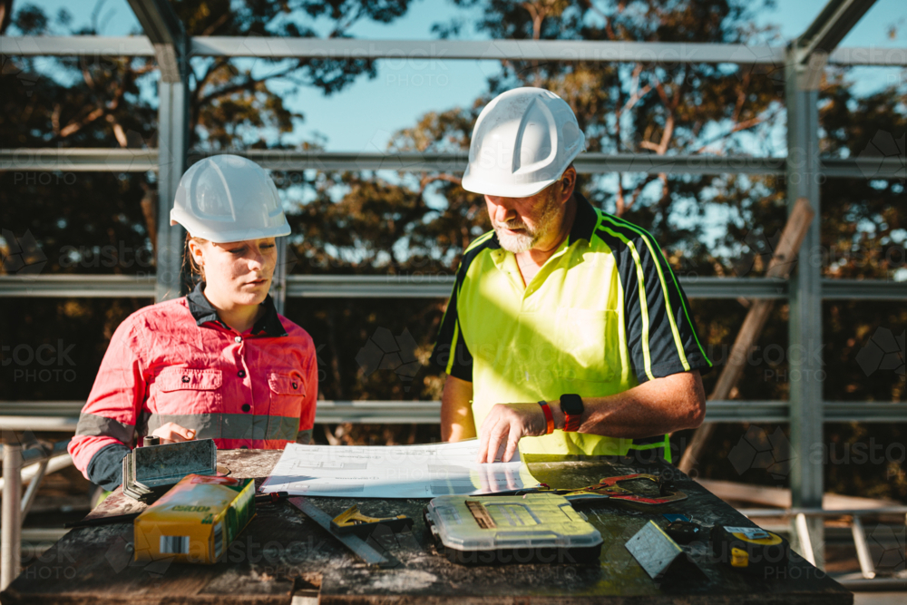 Builders in hardhats looking at the blueprints laid on a flat surface - Australian Stock Image