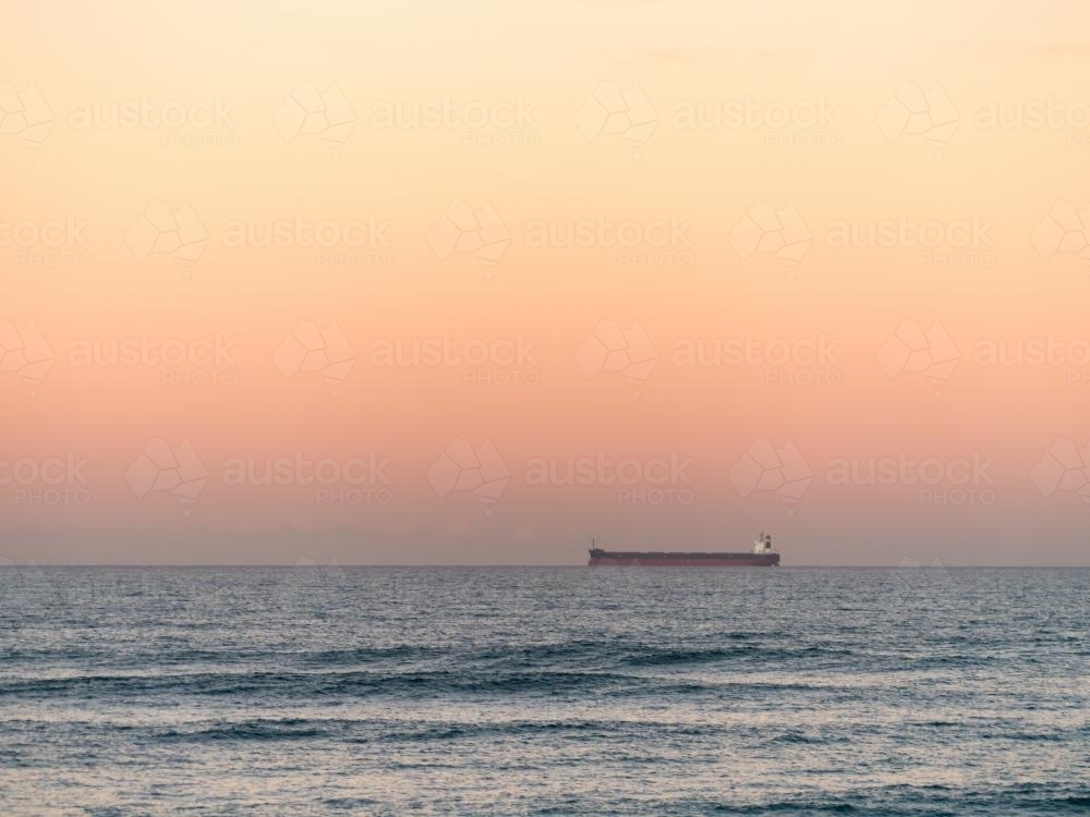 Bulk carrier ship on the horizon with evening blue pink sky - Australian Stock Image