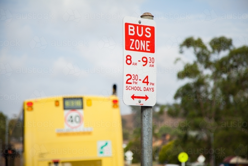 Bus zone street sign with yellow school bus beside it - Australian Stock Image