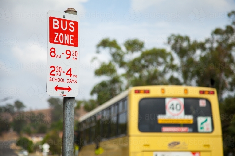 Bus zone street sign with yellow school bus beside it - Australian Stock Image