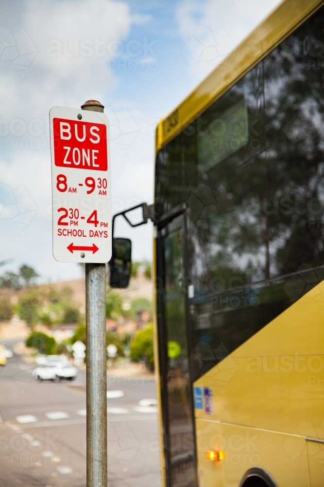 Bus zone street sign with yellow school bus beside it - Australian Stock Image
