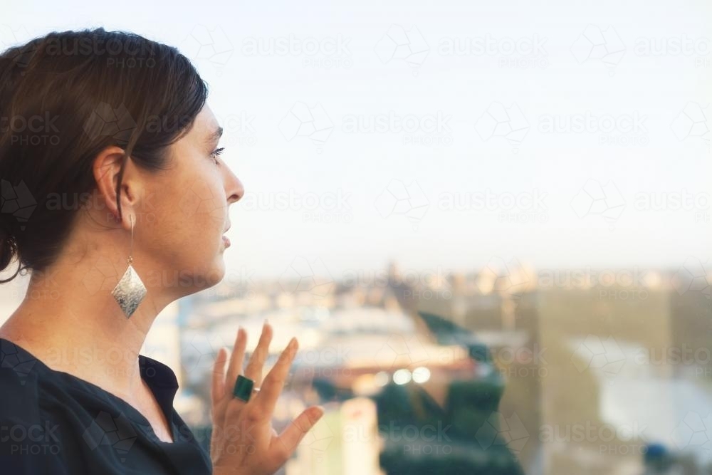 Business woman looking out of city office window - Australian Stock Image