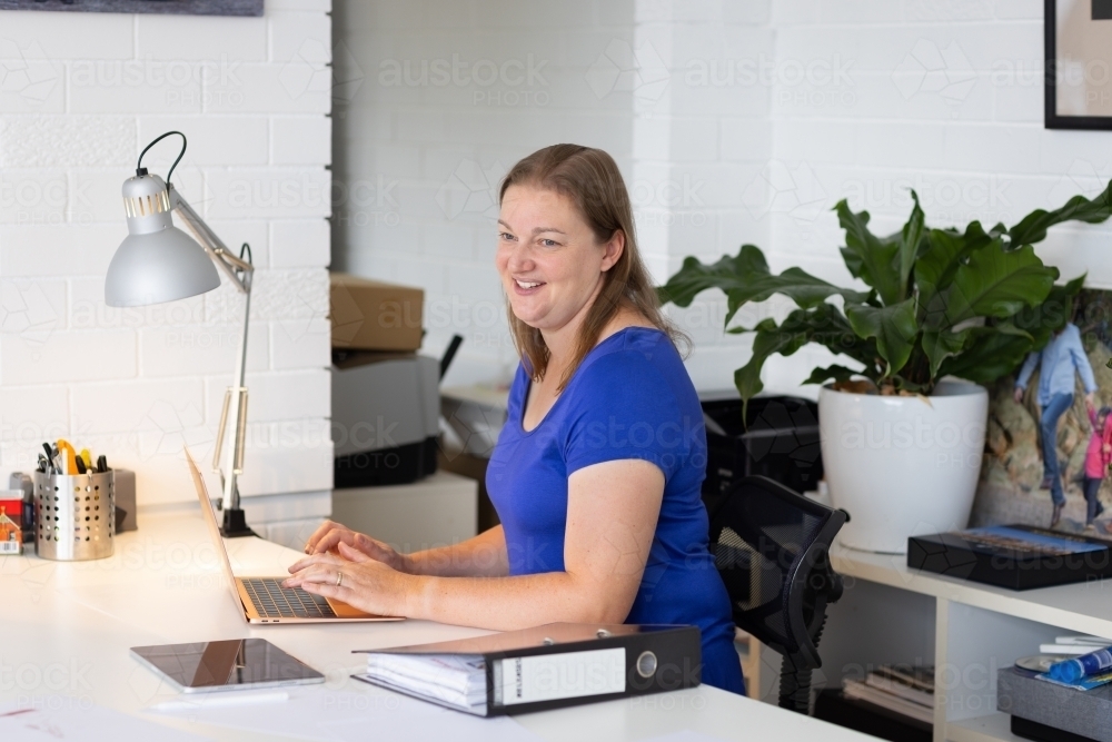 business woman sitting at desk with laptop and file of papers - Australian Stock Image
