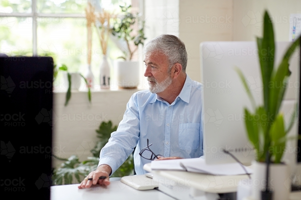 Businessman sitting at a desk in an open office studio - Australian Stock Image