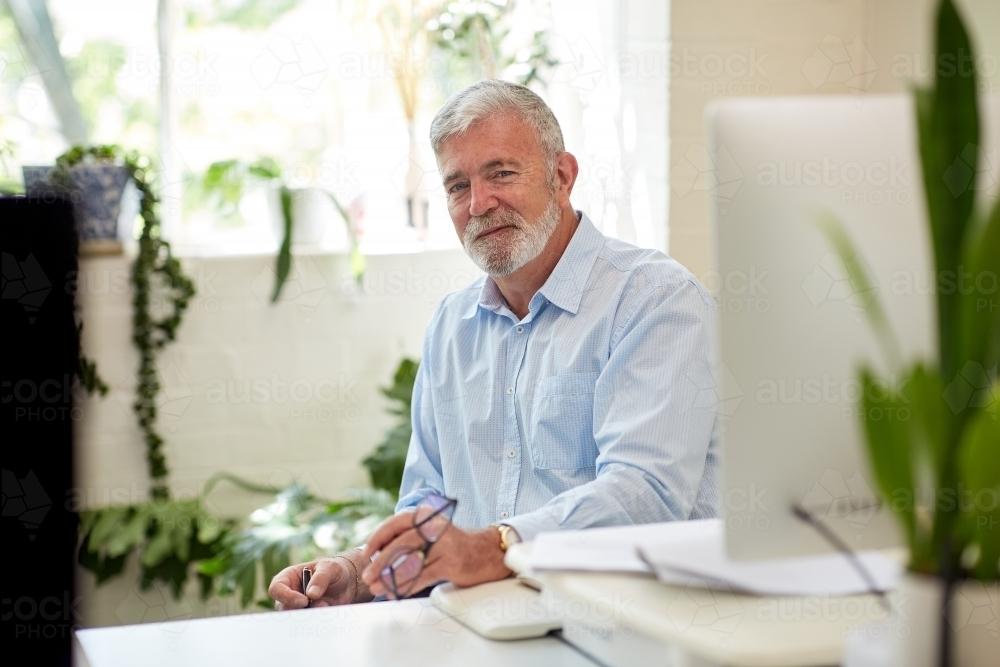 Businessman sitting at a desk in an open office studio - Australian Stock Image