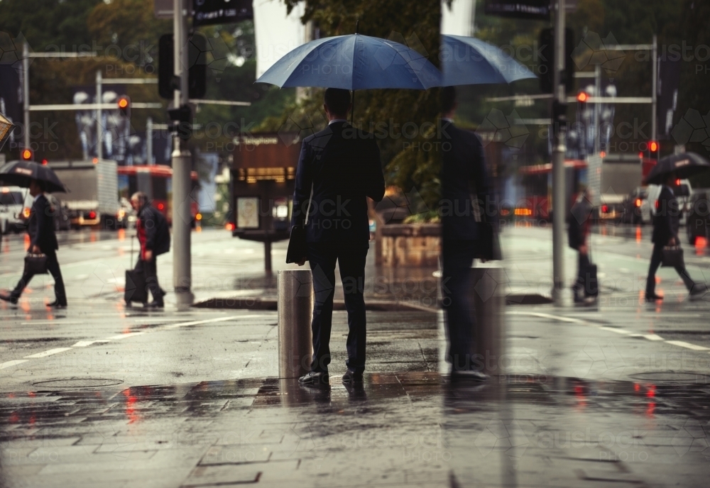Businessman standing in rain with umbrella - Australian Stock Image