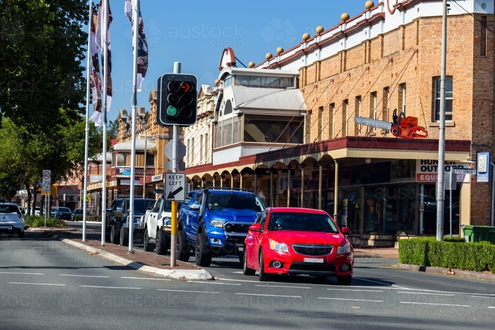 Busy street in town with old buildings beside road red car waiting at traffic light intersection - Australian Stock Image