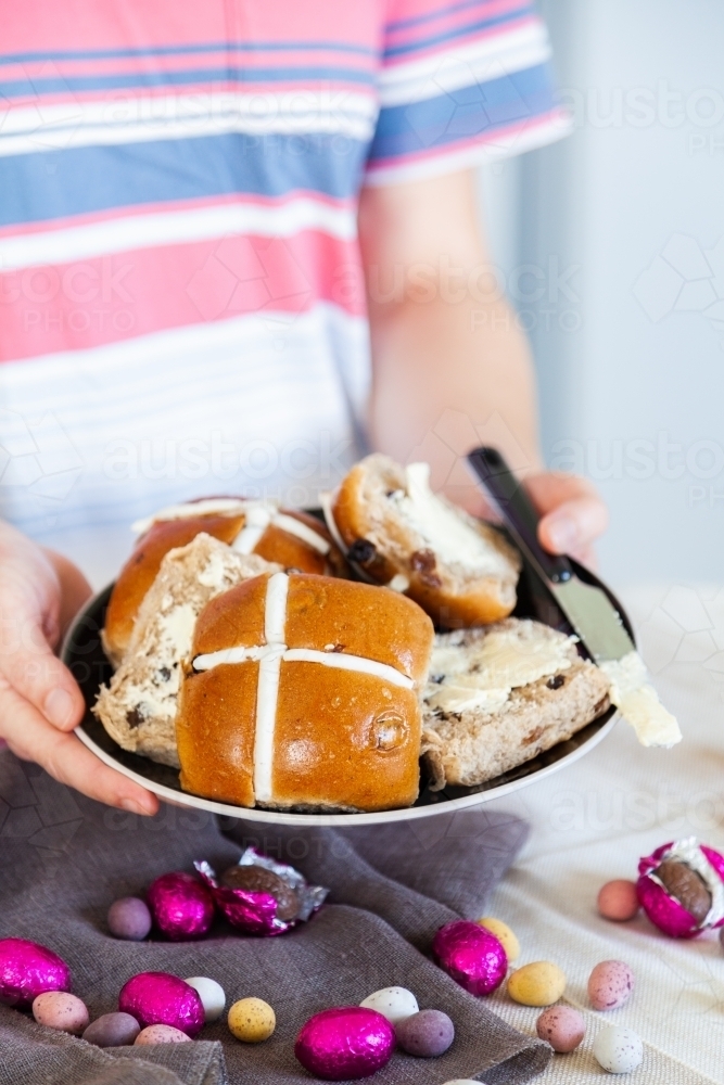 Buttered hot cross buns and scattered eggs at Easter on a plate - Australian Stock Image