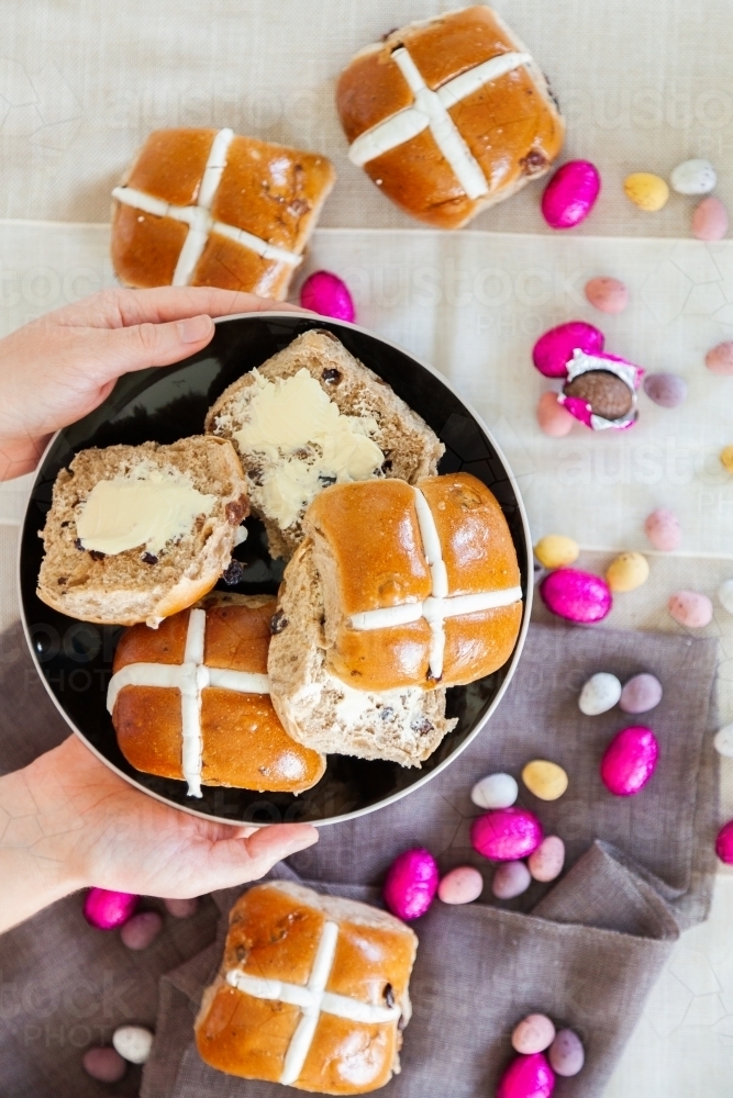 Buttered hot cross buns and scattered eggs at Easter on a plate - Australian Stock Image