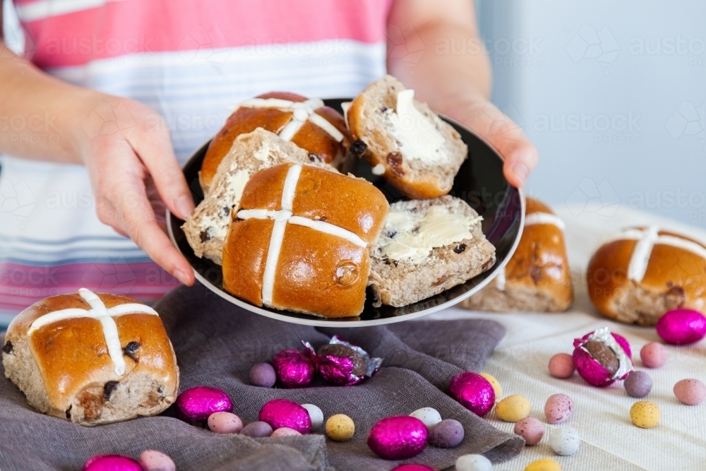 Buttered hot cross buns and scattered eggs at Easter on a plate - Australian Stock Image