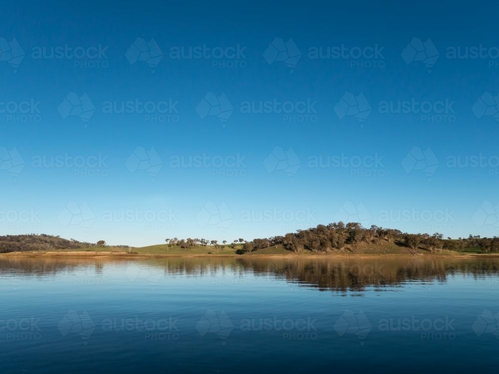 Calm rural water storage dam with a large reflected blue sky - Australian Stock Image
