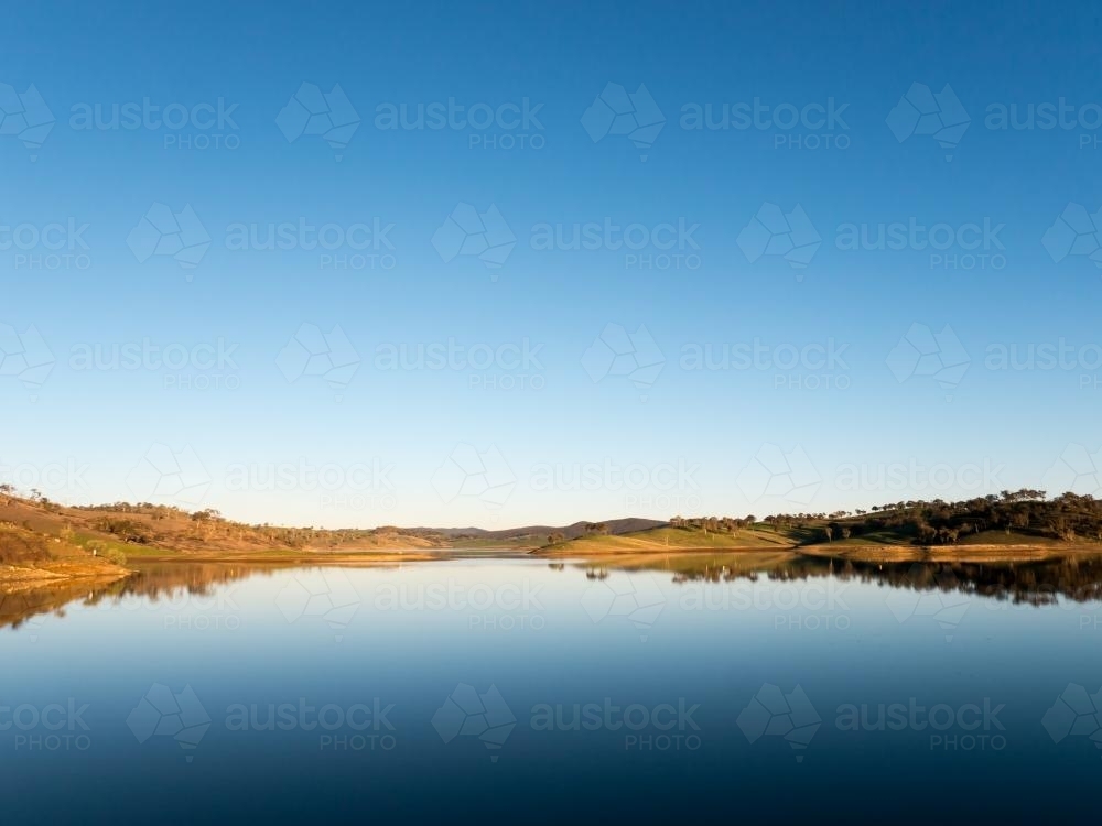 Calm rural water storage dam with a large reflected blue sky - Australian Stock Image