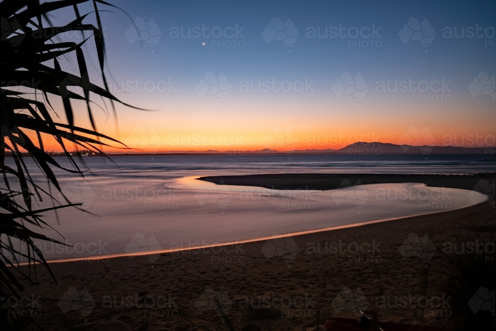 Calm sea with a winding tidal pool reflecting the sky colours - Australian Stock Image